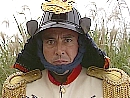 General Tani, wearing a samurai helmet, looks at the camera with an unhappy glare