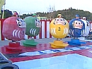 Five contestants are dressed in giant daruma costumes and stand on remote-controlled platforms at the start line of a race track.